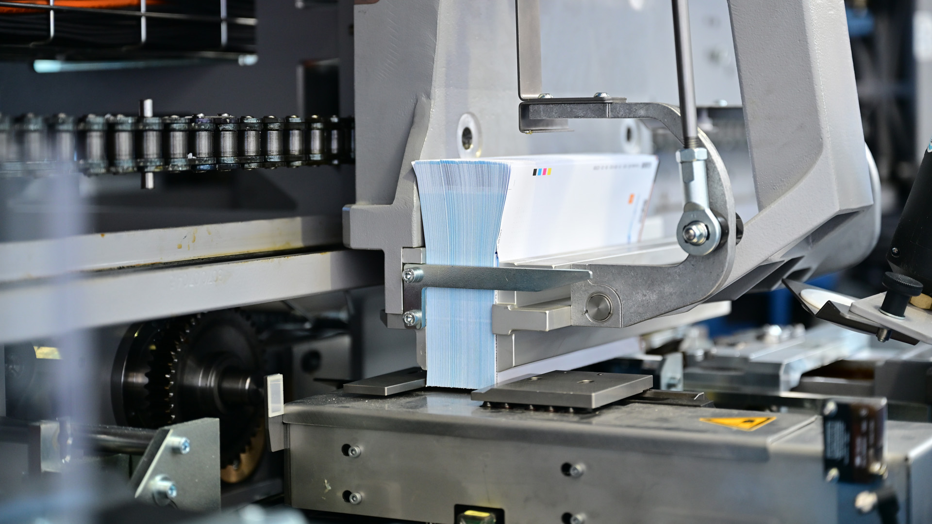 Official MM close-up of the Antaro Digital swing-clamp station gripping a digital book block on its spine — the six-clamp transport that runs the block past the cover/scoring path.