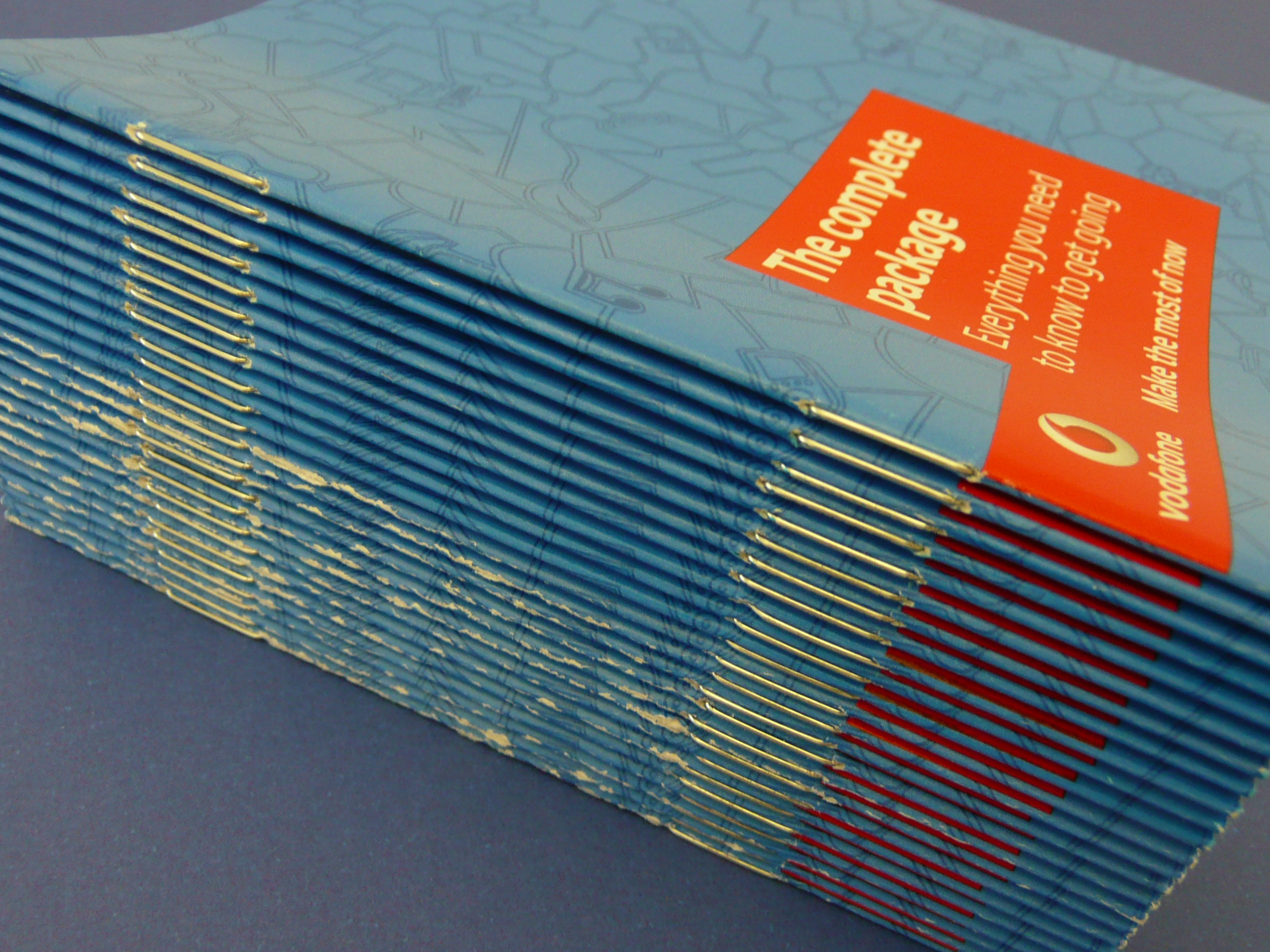 Stack of saddle-stitched Vodafone booklets, wire staples along folded spines