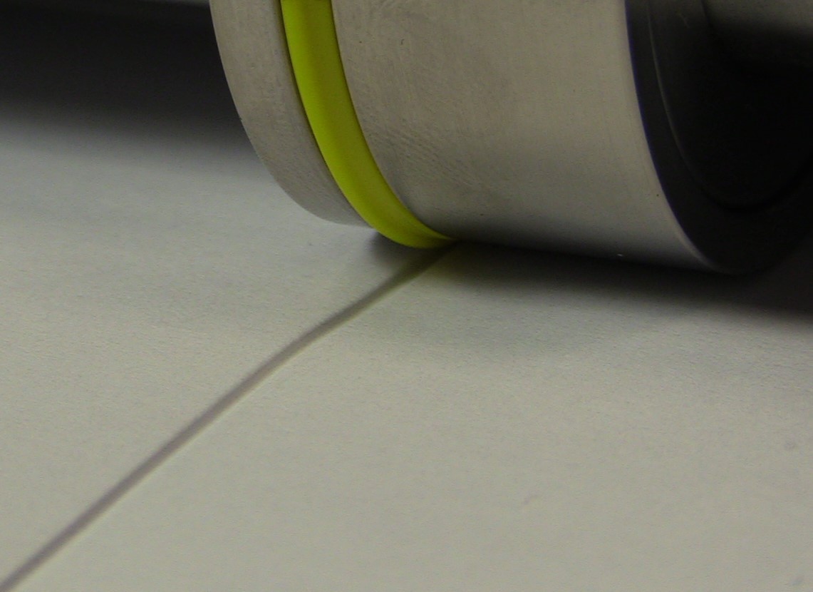 Yellow scoring band pressing a deep, wide score into plain stock